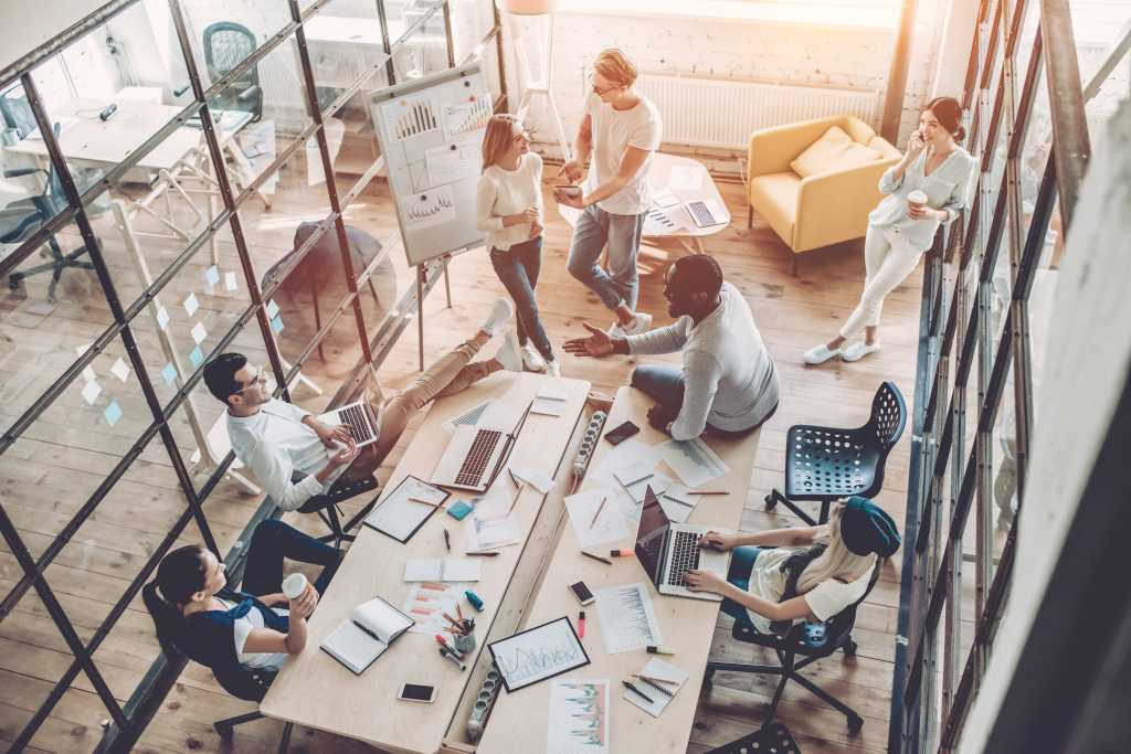 Top view of multiracial young creative people in modern office. Group of young business people are working together with laptop, tablet, smart phone, notebook. Successful hipster team in coworking.